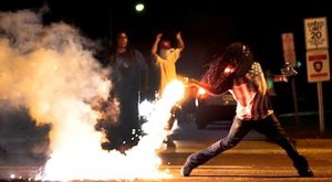 A demonstrator throws back a tear gas container after police officers try to break up a protest in West Florissant, Mo. (Credit: AP)