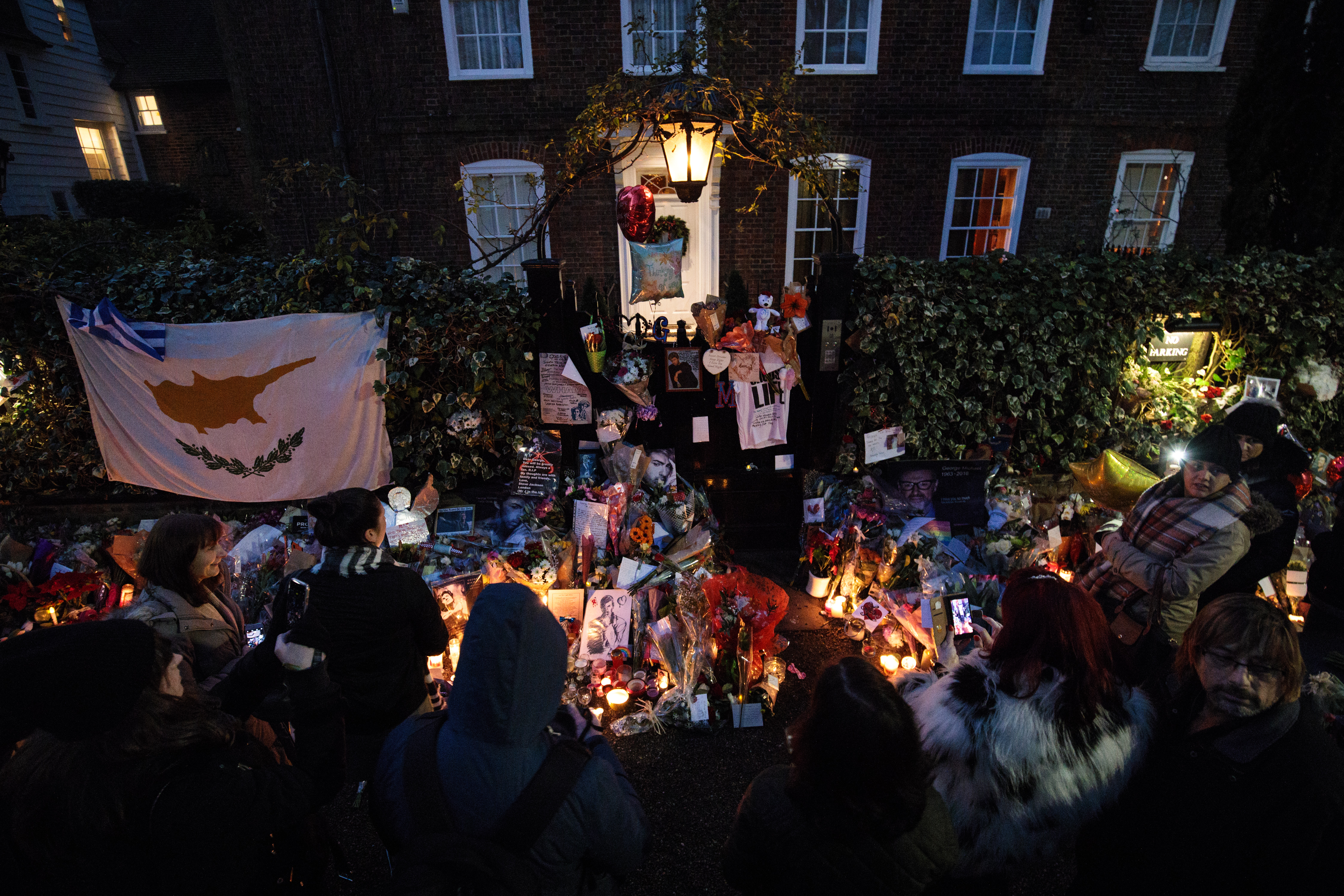 LONDON, ENGLAND - DECEMBER 28: Fans gather in front of tributes of flowers, photographs and candles left outside the home of pop music icon George Michael in The Grove, Highgate on December 28, 2016 in London, England. Singer George Michael died on Christmas day in his country home in Oxfordshire at the age of 53. (Photo by Jack Taylor/Getty Images)