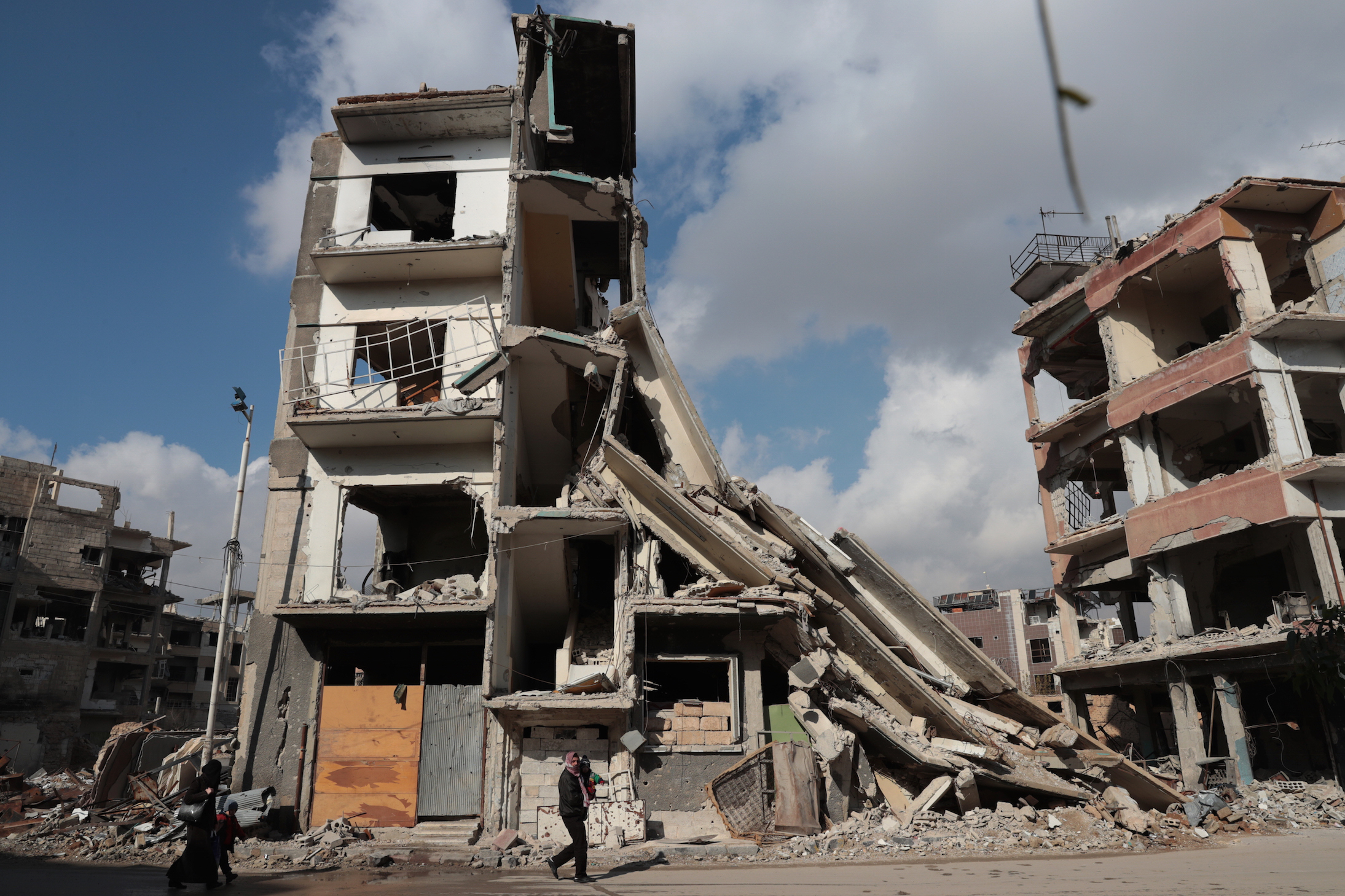 Syrians walk past a destroyed building in the rebel-held town of Douma, on the eastern outskirts of Damascus, on December 30, 2016, on the first day of a nationwide truce. Clashes erupted between Syrian government forces and opposition fighters in an area outside Damascus, despite a nationwide truce that began at midnight, a monitor said. / AFP / Abd Doumany (Photo credit should read ABD DOUMANY/AFP/Getty Images)