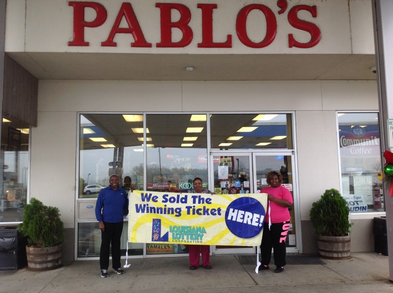 Pablo’s cashiers Samantha Joseph, Joan Samuel and Niesha Johnson hold up a Lottery banner in front of their store on Friday, Jan. 8.