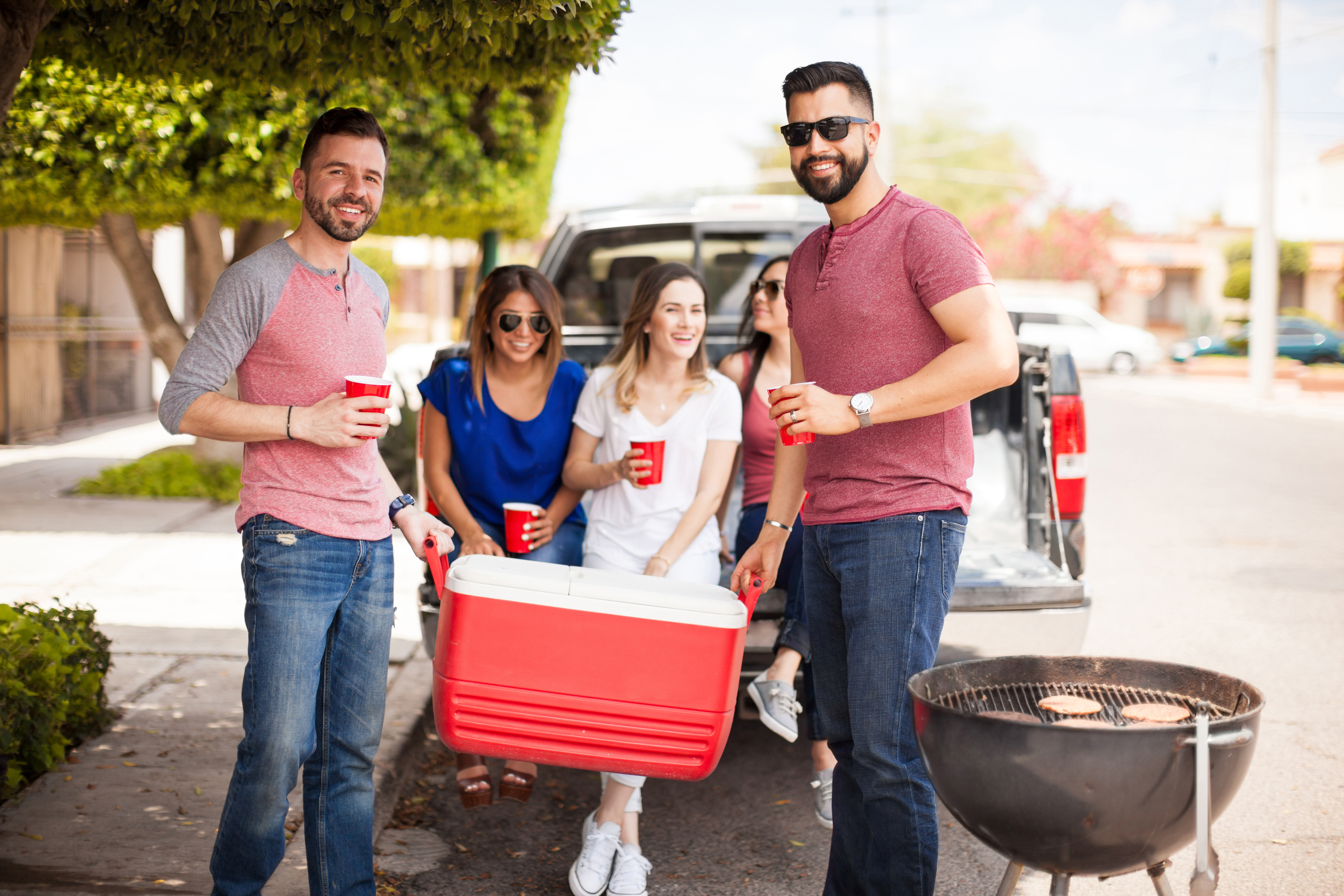 Two attractive young men carrying a cooler full of drinks for a barbecue with friends outdoors