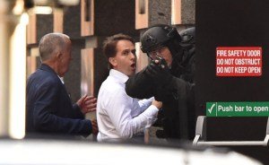 Two hostages run for cover behind a policeman during a hostage siege in the central business district of Sydney on Monday, Dec. 15, 2014. Five people ran out of a Sydney cafe where a gunman has taken hostages and displayed an Islamic flag against the window, police said. (Credit: William West/AFP/Getty Images)