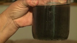 Diane Morita holds up a glass of the black, sludgy liquid on Jan. 26, 2015, that has been coming out of her taps. (Credit: KTLA) 