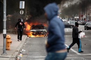 People walk past burning cars near the intersection of Pennsylvania Avenue and North Avenue, April 27, 2015, in Baltimore, Maryland. Riots have erupted in Baltimore following the funeral service for Freddie Gray, who died last week while in Baltimore Police custody. (Credit: Drew Angerer/Getty Images)