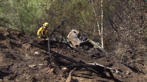 A firefighter is seen near a car that crashed and caught fire in Topanga Canyon on Saturday, April 4, 2015. (Credit: KTLA)