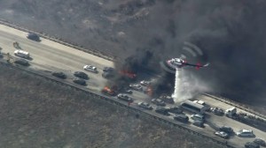 A helicopter drops water on vehicles burning on the 15 Freeway during the North Fire on July 17, 2015. (Credit: KTLA)