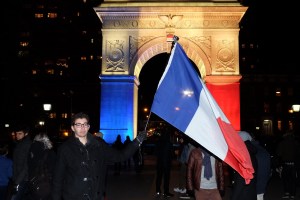 A man waves a flag as the Washington Square Park arch is lit with the French national colors in solidarity with the citizens of France on Saturday, Nov. 14, 2015, in New York, a day after the Paris terrorist attacks. (Credit: Jewel Samad/AFP/Getty Images)