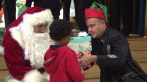 An LAPD officer helps Santa give out gifts to children at Selma Avenue Elementary on Dec. 18, 2015. (Credit: KTLA)