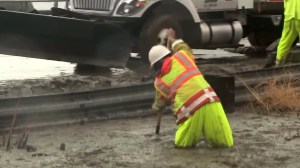 A Caltrans worker tries to clear mud from below the Solimar Fire burn area on Jan. 5, 2016. (Credit: KTLA)