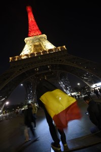 A boy wearing a Belgian flag stands under shows the Eiffel Tower in Paris illuminated in colors of the Belgian flag in tribute to the victims of terrorist attacks in Brussels on March 22, 2016. (Credit: LIONEL BONAVENTURE/AFP/Getty Images)