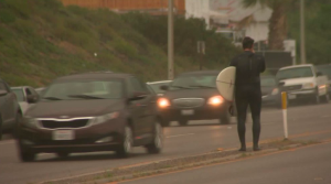 A surfer crosses the street leaving a beach in Malibu as rain begins to fall on March 11, 2016. (Credit: KTLA)