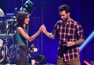 Singers Christina Grimmie and Adam Levine clasp hands onstage during the iHeartRadio Album Release Party with Maroon 5 at the iHeartRadio Theater in Burbank on Aug. 26, 2014. (Credit: Kevin Winter/Getty Images for Clear Channel)