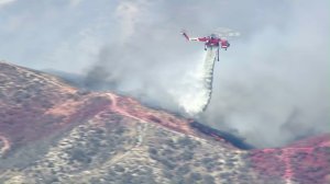 A helicopter drops water on a brush fire in Santa Clarita on July 22, 2016. (Credit: KTLA)