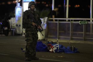 A soldier stands next to a dead body covered with a blue sheet on the Promenade des Anglais seafront in the French Riviera town of Nice on July 15, 2016, after a truck drove into a crowd watching a fireworks display. (Credit: VALERY HACHE/AFP/Getty Images)