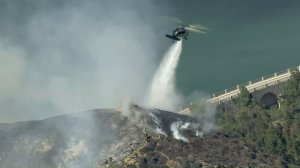 A helicopter drops water on a brush fire burning in the Hollywood Hills on July 19, 2016. (Credit: KTLA)