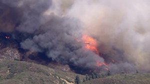 A helicopter makes a water drop on the fast-moving Blue Cut Fire in the Cajon Pass. (Credit: KTLA)