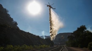 A firefighting helicopter makes water drops to keep errant fires from approaching the train tracks near the 15 Freeway at Keenbrook in San Bernardino County. (Marcus Yam / Los Angeles Times)