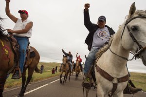 Native Americans ride with raised fists to a sacred burial ground that was disturbed by bulldozers building the Dakota Access Pipeline, near the encampment where hundreds of people have gathered to join the Standing Rock Sioux Tribe's protest of the oil pipeline slated to cross the nearby Missouri River, Sept. 4, 2016 near Cannon Ball, North Dakota. (Credit: ROBYN BECK/AFP/Getty Images)