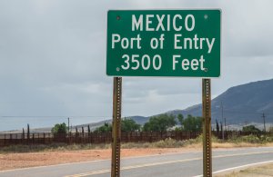 Mexico port of entry highway sign on Highway 92 in Naco Arizona with border fence in the background. (Credit: iStock/Getty Images Plus)