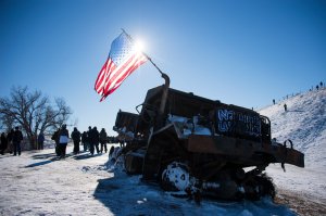 Activists and veterans pass a burnt out dump truck as they depart a police barricade on a bridge near Oceti Sakowin Camp on the edge of the Standing Rock Sioux Reservation on Dec. 4, 2016, outside Cannon Ball, North Dakota. (Credit: JIM WATSON/AFP/Getty Images)