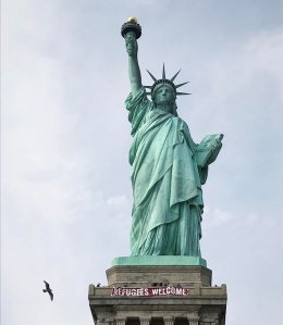 A 20-foot red and white banner that read "Refugees welcome" hung across the Statue of Liberty on Tuesday, Feb. 21, 2017. (Credit: Vitória Londero)