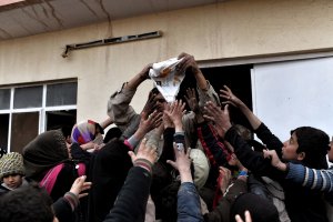 An Iraqi soldier delivers aid to displaced residents of Mosul at a gasoline station, used as a gathering point, after fleeing Mosul on March 3, 2017, during an offensive by security forces to retake the western parts of the city from Islamic State group fighters. (Credit: Aris Messinis / AFP / Getty Images)