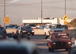 Motorists wave as police cars pursue the Ford Bronco driven by Al Cowlings, carrying O.J. Simpson, on a 90-minute slow-speed car chase June 17, 1994 on the 405 freeway in Los Angeles. (Credit: MIKE NELSON/AFP/Getty Images)