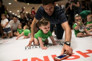 A father lures his child along with an iPhone during warmups before babies race in the NYC Triathlon's annual Diaper Derby, July 14, 2017, in New York City. (Credit: Dominick Reuter / AFP / Getty Images)