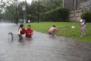 A man helps children across a flooded street as they evacuate their home after the area was inundated with flooding from Hurricane Harvey on Aug. 27, 2017, in Houston, Texas. (Credit: Joe Raedle / Getty Images)