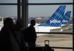 Travelers walk past the tails of JetBlue airplanes in the airport terminal at Ronald Reagan Washington National Airport in Arlington, Virginia, Dec. 22, 2016. (Credit: SAUL LOEB/AFP/Getty Images)