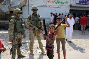 A picture taken during a press tour provided by the Russian Armed Forces on Sept. 15, 2017, shows Russian soldiers standing guard in a central street in Syria's eastern city of Deir Ezzor, as local children pose nearby. (Credit: Dominique Derda / AFP / Getty Images)