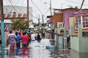 People walk in a flooded street next to damaged houses in Catano, Puerto Rico, on Sept. 21, 2017. (Credit: Hector Retamal / AFP / Getty Images)