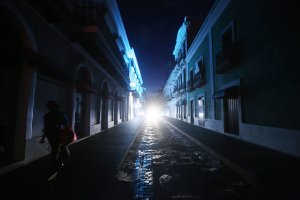 A woman walks down a darkened street past historic buildings in the touristic Old San Juan neighborhood, on October 13, 2017 in San Juan, Puerto Rico. (Credit: Mario Tama/Getty Images)