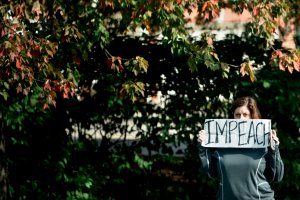 A protester holds an "impeach" sign outside the Trump National Golf Course as a motorcade with US President Donald Trump arrives in Sterling, Virginia, on October 28, 2017. (Credit: Brendan Smialowski/AFP/Getty Images)