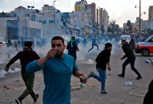 Palestinian protesters run for cover from tear gas during clashes with Israeli troops near the West Bank city of Ramallah at a Dec. 7, 2017, protest against President Donald Trump's decision to recognize Jerusalem as the capital of Israel. (Credit: AFP PHOTO / ABBAS MOMANI)