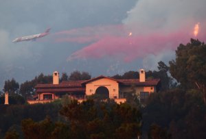 A plane drops flame retardant on a luxury hillside home in the Santa Barbara area threatened by the Thomas Fire on Dec. 11, 2017. (Credit: Robyn Beck / AFP / Getty Images)