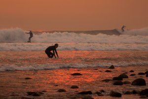 A smoke-filled sky filters orange light around surfers as the Thomas Fire continues to grow and threaten communities on Dec. 12, 2017, in Carpinteria. (Credit: David McNew / Getty Images)