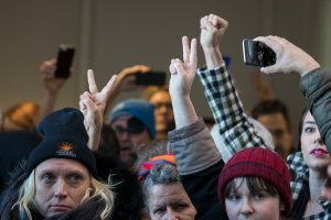 Demonstrators hold up two fingers signaling their second verbal warning from U.S. Capitol Police officers who are ordering the protesters to disperse during a demonstration against Republican tax reform legislation outside the office of Senator Lisa Murkowski, in the Hart Senate Office Building on Capitol Hill, on Dec. 13, 2017. (Credit: ALEX EDELMAN / AFP / Getty Images)