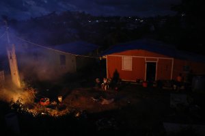 A resident sits outside her home, which lacks electricity, as a trash fire burns on December 21, 2017 in San Isidro, Puerto Rico. (Credit: Mario Tama/Getty Images)