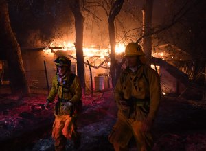 Firefighters move away from a burning house after discovering downed live power lines, as the Thomas wildfire continues to burn in Carpinteria, California, on Dec. 10, 2017. (Credit: Mark Ralston / AFP / Getty Images)