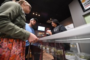 Tourists Laura Torgerson and Ryan Sheehan, visiting from Arizona, talk to a budtender at the Green Pearl Organics dispensary on the first day of legal recreational marijuana sales in California on Jan. 1, 2018 in Desert Hot Springs. (Credit: ROBYN BECK/AFP/Getty Images)