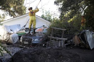 A Cal Fire firefighter looks through a car next to a Montecito home that was destroyed by a mudslide, Jan. 12, 2018. (Credit: Justin Sullivan / Getty Images)