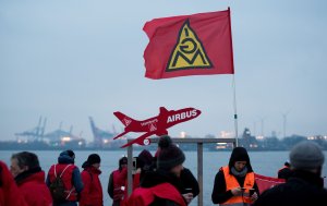 Members of the metalworkers' and electrical industry union (IG Metall) hold an Ig Metall flag and a placard displaying an Airbus plane during a warning strike near a ferry dock in Teufelbrueck, northern Germany on February 02, 2018. (Credit: DANIEL REINHARDT/AFP/Getty Images)