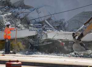 A crushed vehicle is seen near a worker as authorities investigate the scene where a pedestrian bridge collapsed a few days after it was built near Florida International University in Miami, March 16, 2018. (Credit: Joe Raedle / Getty Images)