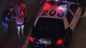 A woman is seen being handcuffed at the scene where a car crashed in the city of Industry following a pursuit earlier on March 27, 2018. (Credit: KTLA)