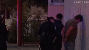 A police officer at the scene of a shooting at a motel in North Hollywood handcuffs a man seen standing and facing a wall. (Credit: Loud Labs)