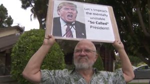 A protestor in Santa Monica is seen holding a sign stating opposition to President Donald Trump during the president's first visit to the state on March 13, 2018. (Credit: KTLA)