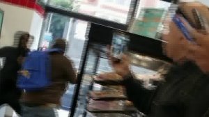A blurred still from cell phone video shows a man, who is wearing a blue backpack, being beaten by two other people inside a 7-Eleven convenience store in downtown Los Angeles on May 1, 2017. (Credit: Myra Olvera)