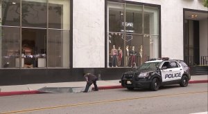 A crime analysts inspects a window that was apparently smashed during a robbery at the Saks Fifth Avenue in Beverly Hills on May 21, 2018. (Credit: KTLA)