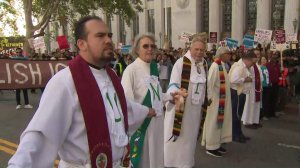 Clergy members join hands to block Spring Street as they protest the Trump administration's "zero tolerance" immigration policy as Attorney General Jeff Sessions visits Los Angeles on June 26, 2018. (Credit: KTLA)